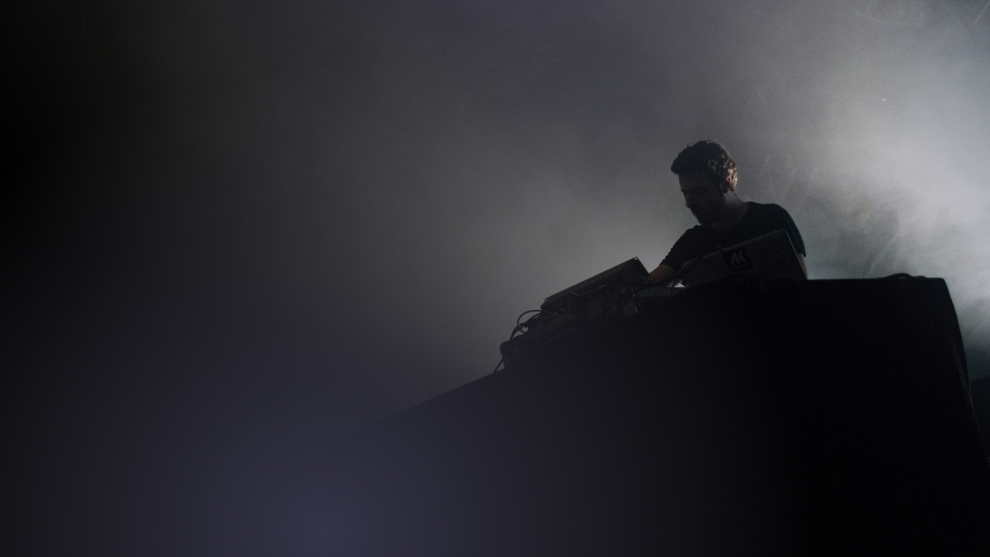 "alt=A DJ on stage backlit during a festival, a metaphor for negotiations and headliners' fees."